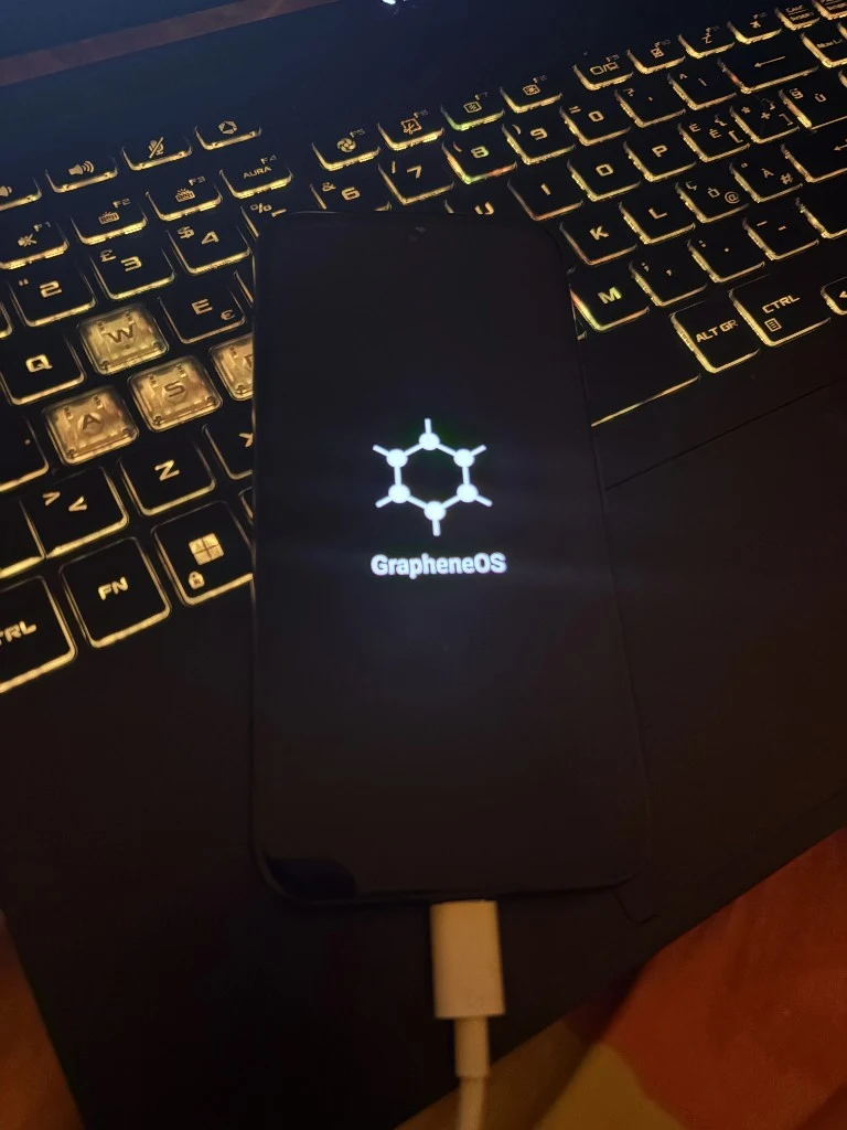 Google Pixel displaying the GrapheneOS boot logo while connected by USB to a laptop keyboard